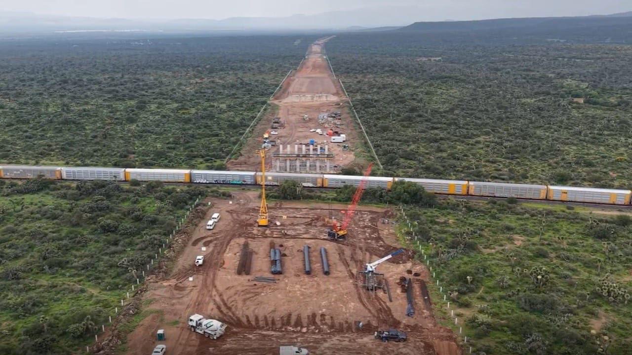 Construcción de una autopista en San Luis Potosí con maquinaria y un tren de carga al fondo.