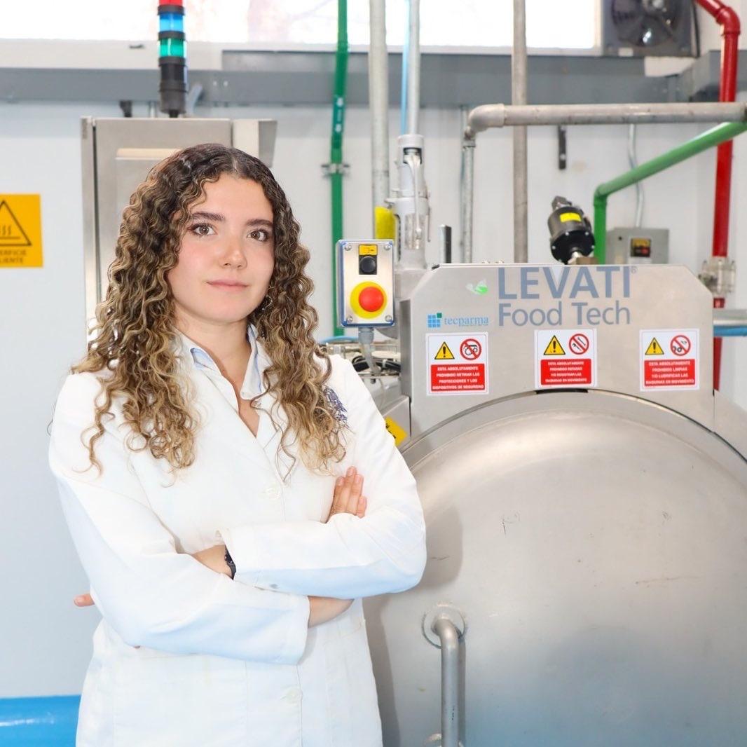 Alejandra de la Torre, egresada de la UASLP, en un laboratorio de ciencia de alimentos junto a equipo industrial.