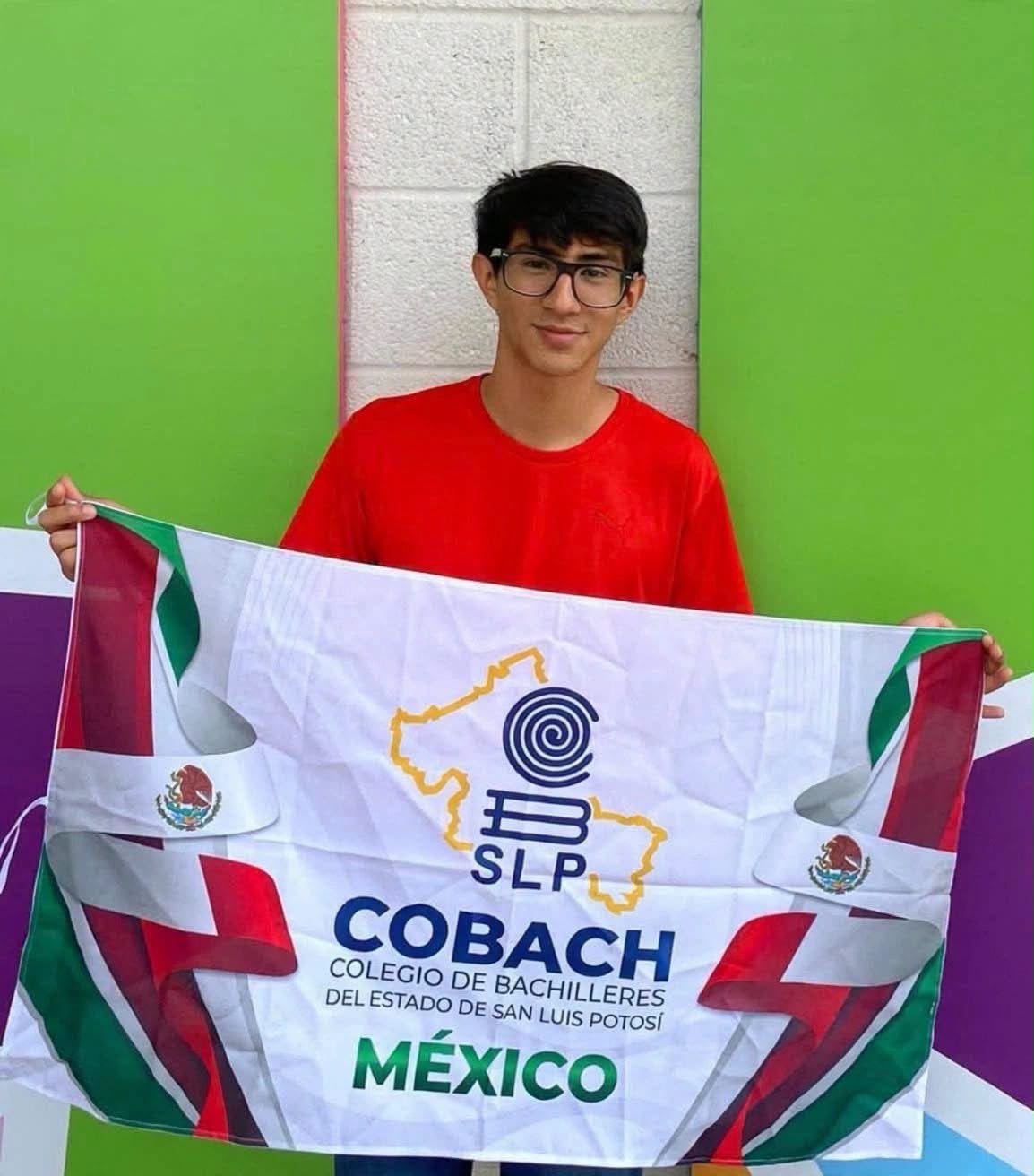 José Andrés Zamora Moncada, exalumno del Cobach, sostiene una bandera del Colegio de Bachilleres de San Luis Potosí tras obtener medalla de oro en matemáticas.