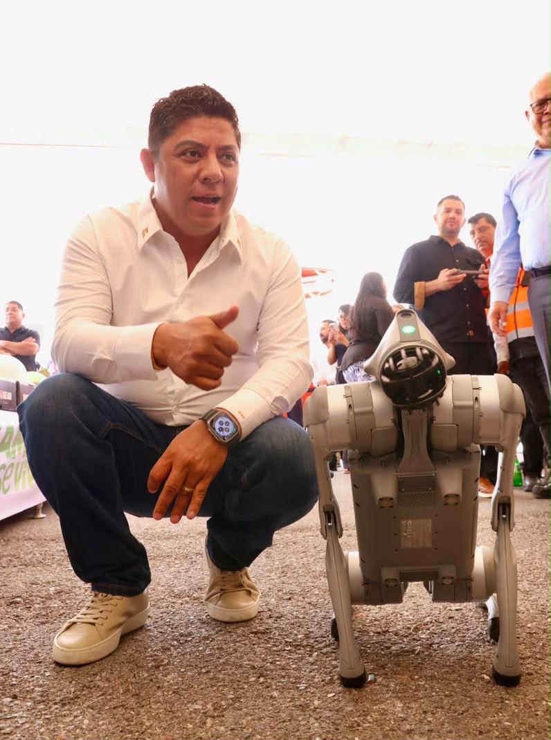 Ricardo Gallardo Cardona junto a un perro robot durante la presentación de tecnología de seguridad para la FENAPO 2026.