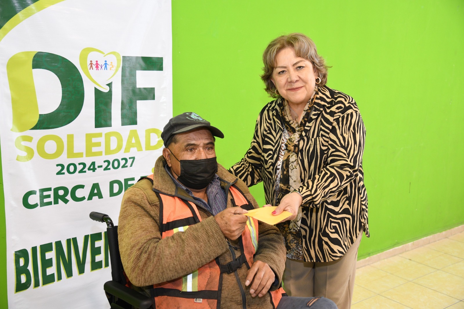 María del Pilar Cardona Reyna entrega un apoyo a una persona usuaria de silla de ruedas en instalaciones del DIF de Soledad.