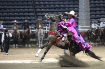 Integrante de una escaramuza charra montada a caballo durante una presentación en la Arena Potosí, con otros participantes al fondo.