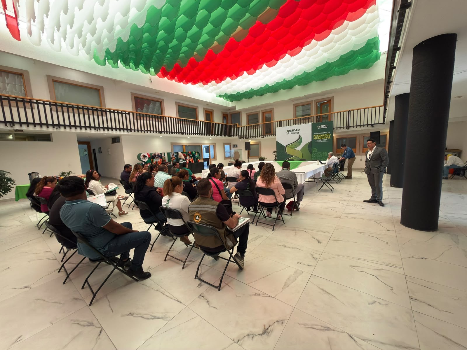 Funcionarios y asistentes participan en reunión sobre la Guía Consultiva de Desempeño Municipal en un patio institucional decorado con motivos tricolores.