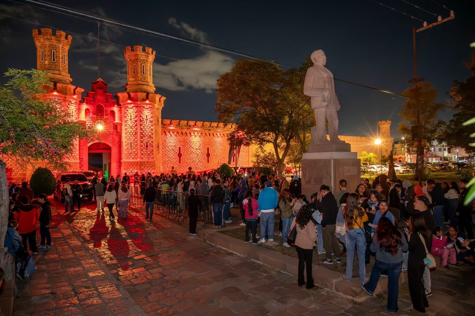 Vista nocturna de la fachada iluminada del Centro de las Artes de San Luis Potosí, con visitantes reunidos frente al recinto.